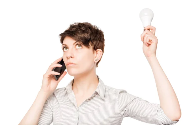 Chica con el teléfono y la lámpara en las manos posando sobre un fondo blanco —  Fotos de Stock