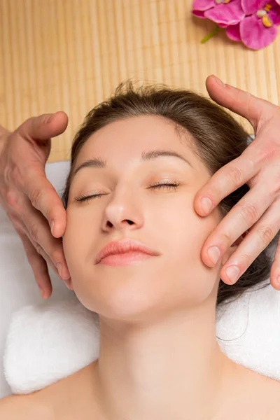 Le visage d'une jeune femme, la peau tendue et les mains du masseur — Photo