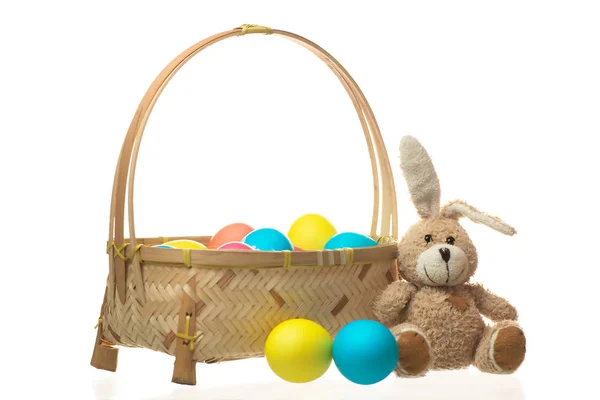 Teddy rabbit near a basket of colorful Easter eggs isolated on w — Stock Photo, Image