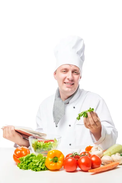 Vertikální portrét kuchaře u stolu s knihou a zeleniny — Stock fotografie