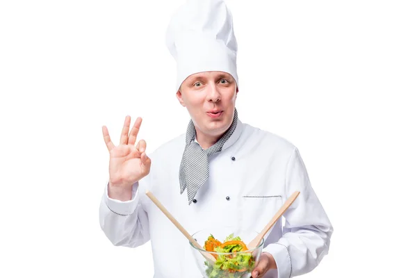 Admirando chef con ensalada en las manos mostrando gesto de mano en un abrir y cerrar de ojos — Foto de Stock