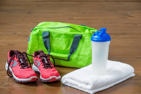 Grüne Sporttasche und rosa Turnschuhe neben einem Handtuch mit einer Flasche Wasser — Stockfoto