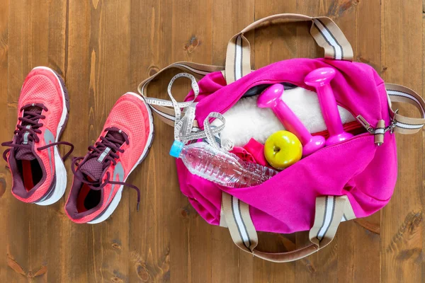 Bolsa de deporte abierta y zapatos de correr rosa en un piso de madera superior vie — Foto de Stock