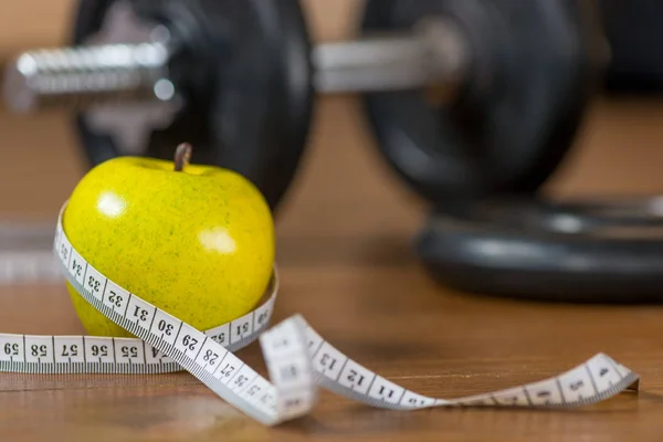 Apple in focus and centimeter against the background of dumbbell — Stock Photo, Image