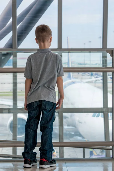 De jongen op de luchthaven bewondert het vliegtuig buiten het raam — Stockfoto