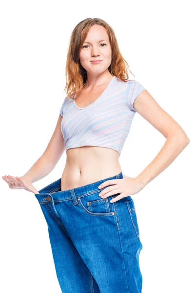 Štíhlé rusovlasá dívka ukazuje staré kalhoty po hubnutí na — Stock fotografie