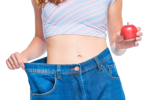 Tunn flicka i gamla jeans med ett äpple i handen på en vit baksida — Stockfoto