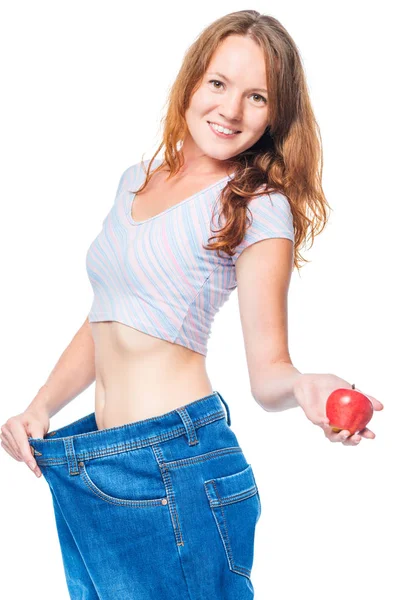 Beautiful smiling girl with an apple in her hand and big jeans o — Stock Photo, Image