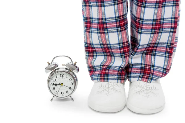 Reloj despertador y piernas femeninas en pijama y zapatillas en una b blanca — Foto de Stock