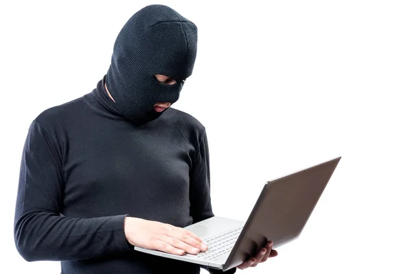 Um hacker em roupas pretas e uma máscara com um laptop em uma ba branca — Fotografia de Stock