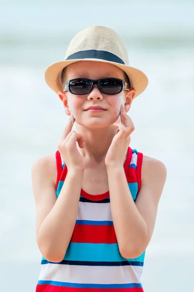 Băiatul de pe plajă purtând o pălărie și ochelari își frotiază pielea cu — Fotografie, imagine de stoc