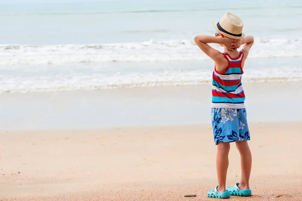 Niño 7 años en una camiseta y pantalones cortos mira el mar en la playa —  Fotos de Stock