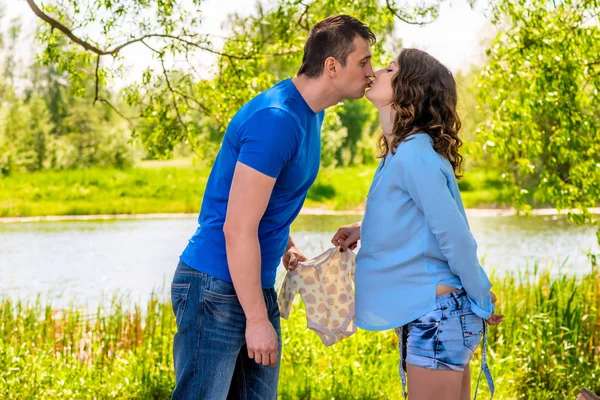 Беременная женщина и ее муж целуются в парке у озера — стоковое фото
