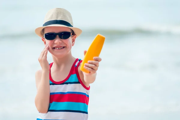 Boy in a hat and sunglasses protects the skin with cream from th — Stock Photo, Image