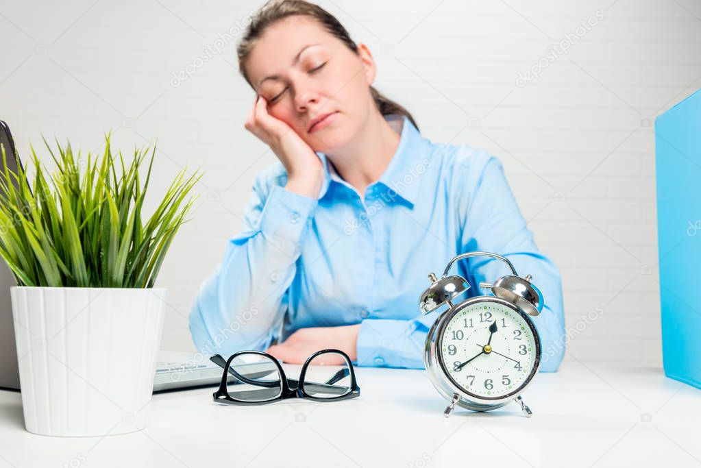 Asleep businesswoman in an office out of focus, alarm clock clos