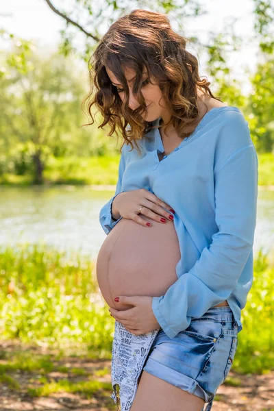 Jonge zwangere vrouw haar buik knuffelen met haar handen, portret — Stockfoto