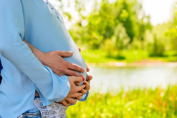 Pancia di una donna incinta abbracciata da un lago nel parco — Foto Stock