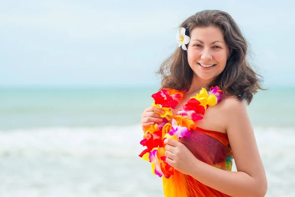 Gelukkig jonge brunette in pareo en bloem lei tegen de zee — Stockfoto