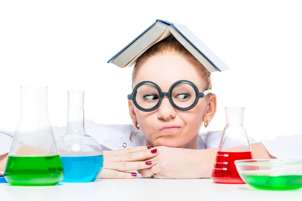 Thoughtful crazy chemist with a book on her head looking at test — Stock Photo, Image