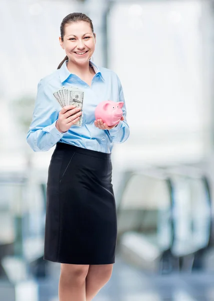 Счастливая деловая женщина держит копилку и доллары в офисе — стоковое фото