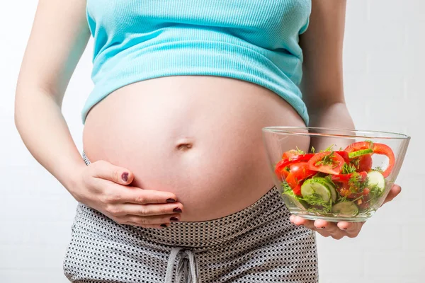 Bauch einer schwangeren Frau und eine Schüssel Gemüsesalat in Großaufnahme — Stockfoto