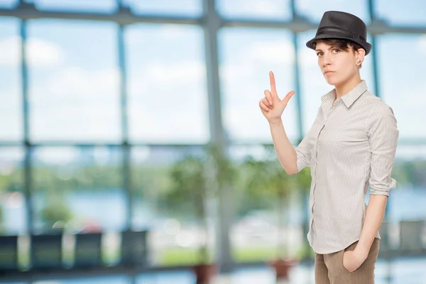 Serious girl holds fingers pistol and wears a black hat in the o — Stock Photo, Image