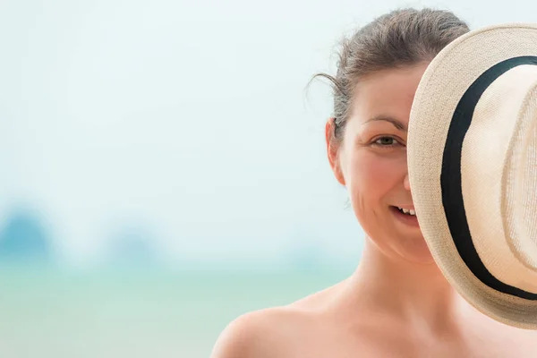 Žena na pláži pokrývá polovinu obličeje s kloboukem — Stock fotografie