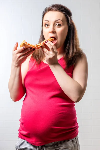 Голодна вагітна жінка з великим шматочком піци на цеглі — стокове фото