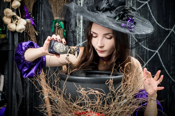 Čarodějnice v černém klobouku v hrnci uvaří lektvar — Stock fotografie