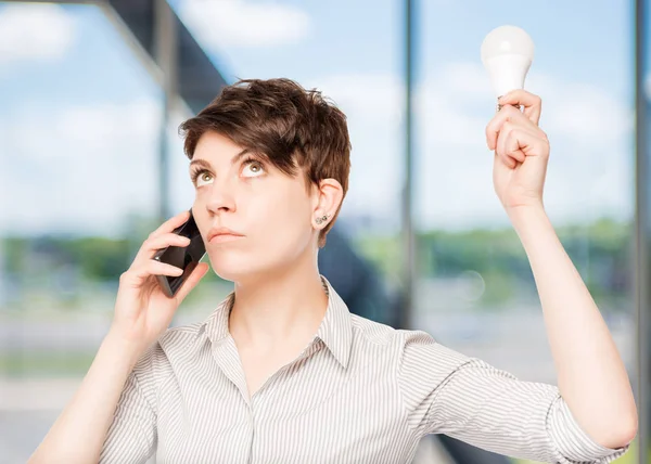 Ragazza con telefono e lampada tra le mani in posa in ufficio — Foto Stock