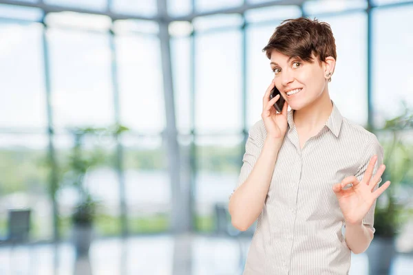 Young brunette with a phone in the office — Stock Photo, Image