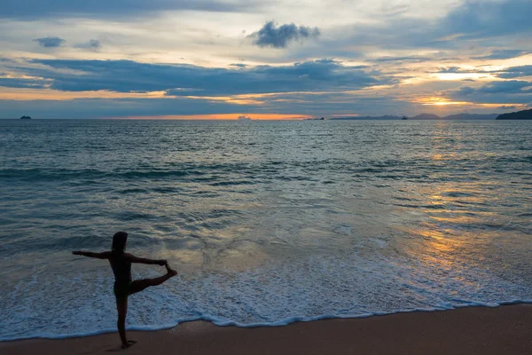 ผู้หญิงที่กําลังเล่นโยคะบนชายหาดตอนพระอาทิตย์ตก — ภาพถ่ายสต็อก