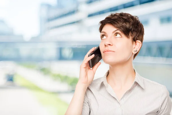 Mujer con un teléfono mirando el espacio en blanco en la oficina —  Fotos de Stock