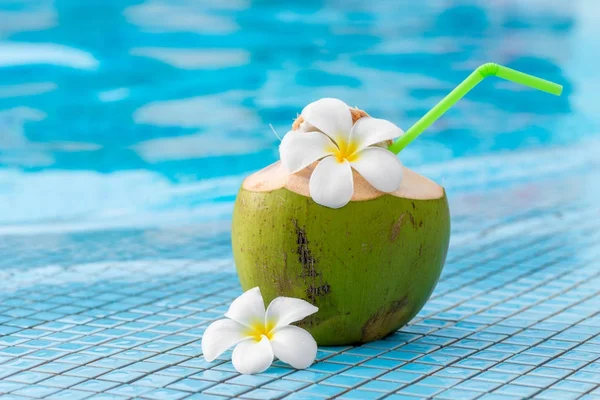 Close-up of a green coconut with a straw on the edge of a pool — Stock Photo, Image