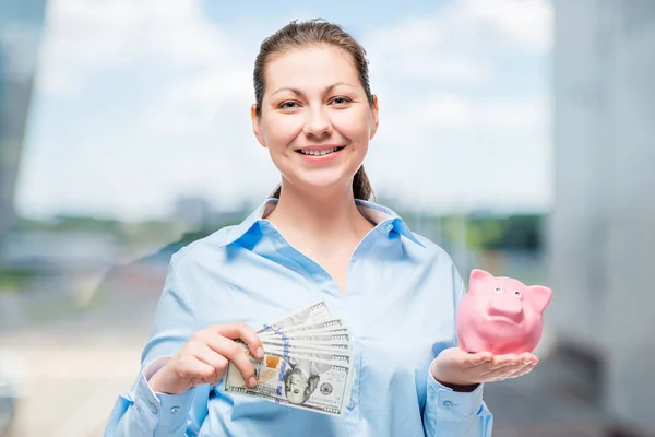 Mujer feliz en camisa azul con dólares y alcancía en la oficina — Foto de Stock