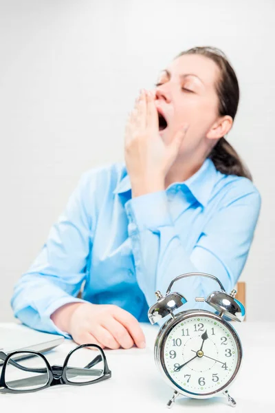 Cansada bocejando mulher em um escritório fora de foco e um despertador — Fotografia de Stock
