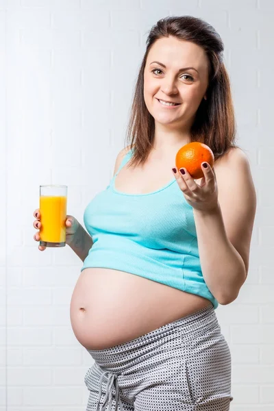 Ein Mädchen mit einer Orange und einem Glas Saft ist glücklich, sie ist Preg — Stockfoto