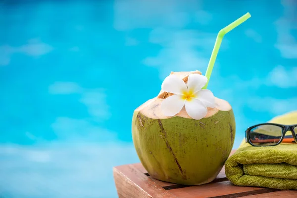 Coconut with a straw on the edge of a deckchair against a blue w — Stock Photo, Image