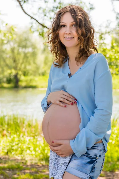 Portret van een gelukkig toekomstige moeder in een park in de buurt van het meer — Stockfoto