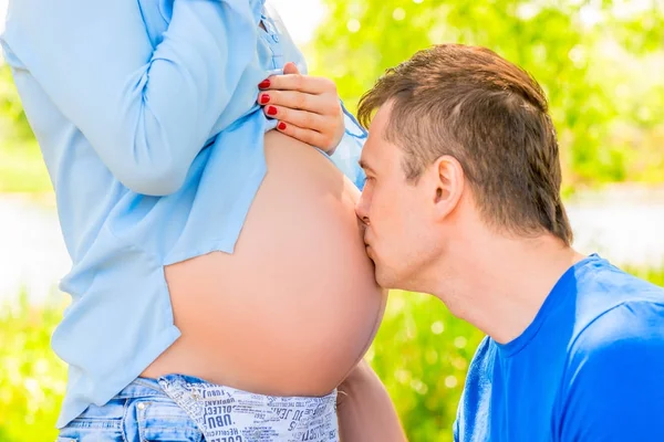 Homem feliz beija a barriga de sua esposa grávida no parque — Fotografia de Stock