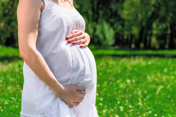 Pancia di una donna incinta in un vestito bianco su uno sfondo di un — Foto Stock