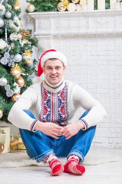 Trevlig man i en tröja och nyår strumpor sitter nära en Kristus — Stockfoto