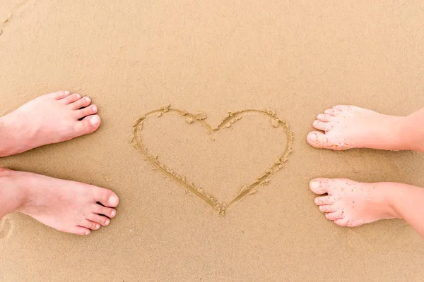 Jambes couple amoureux pieds nus sur le sable près du motif de coeur — Photo