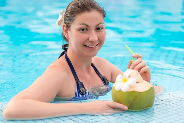 Счастливая женщина наслаждается вкусным кокосовым молоком в бассейне — стоковое фото
