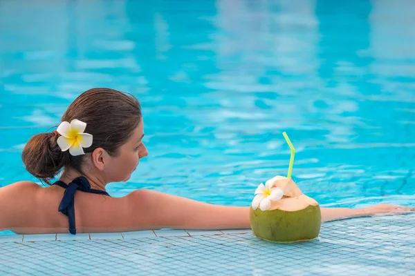 Расслабляющая женщина в бикини в бассейне с сочным кокосом — стоковое фото