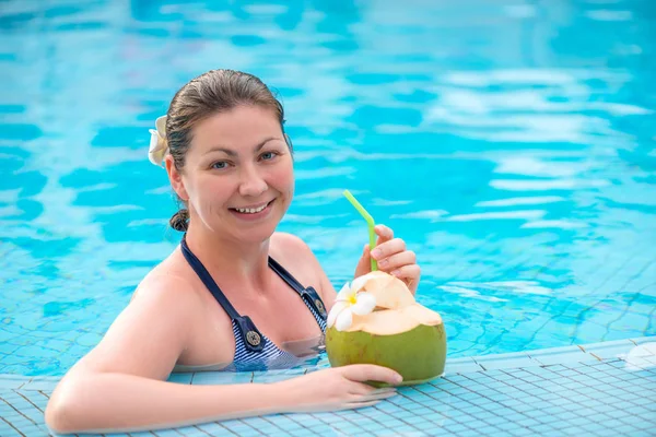 Gelukkig brunette met kokos rusten in het zwembad in de tropen — Stockfoto
