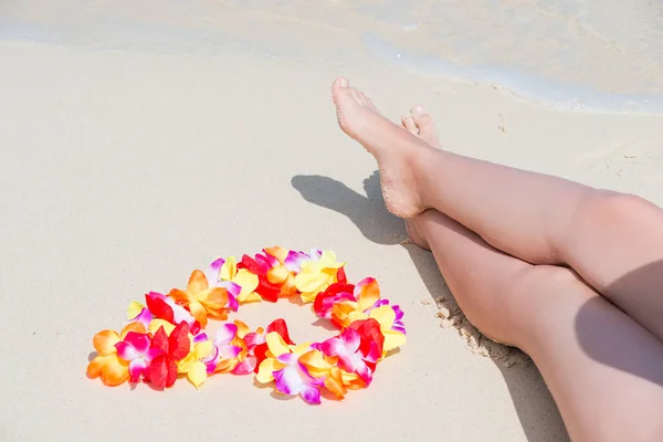 Beautiful female legs on a sandy beach and Hawaiian Lei close-up — Stock Photo, Image