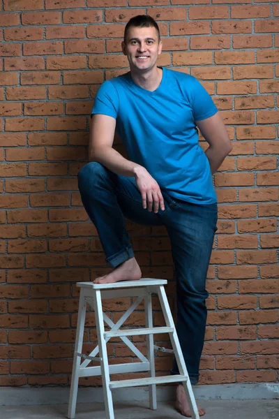 brutal barefoot man in a chair posing against a brick wall backg