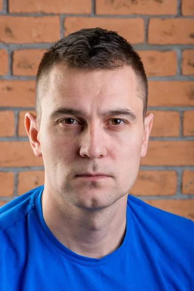 Portrait of brutal brunette in blue t-shirt on brick wall backgr — Stock Photo, Image