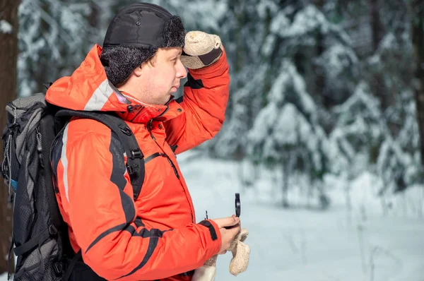 En man med en ryggsäck och en kompass gick vilse i en snöig skog — Stockfoto